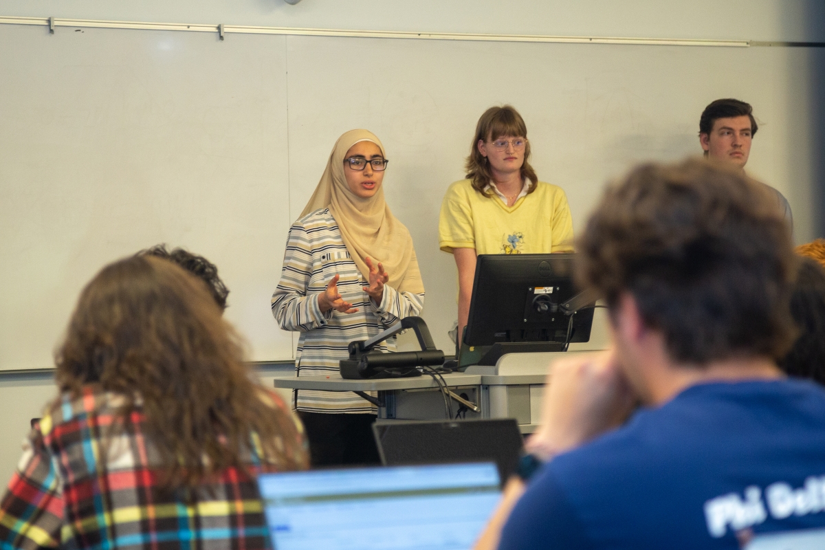 Three students stand while giving a presentation in a classroom